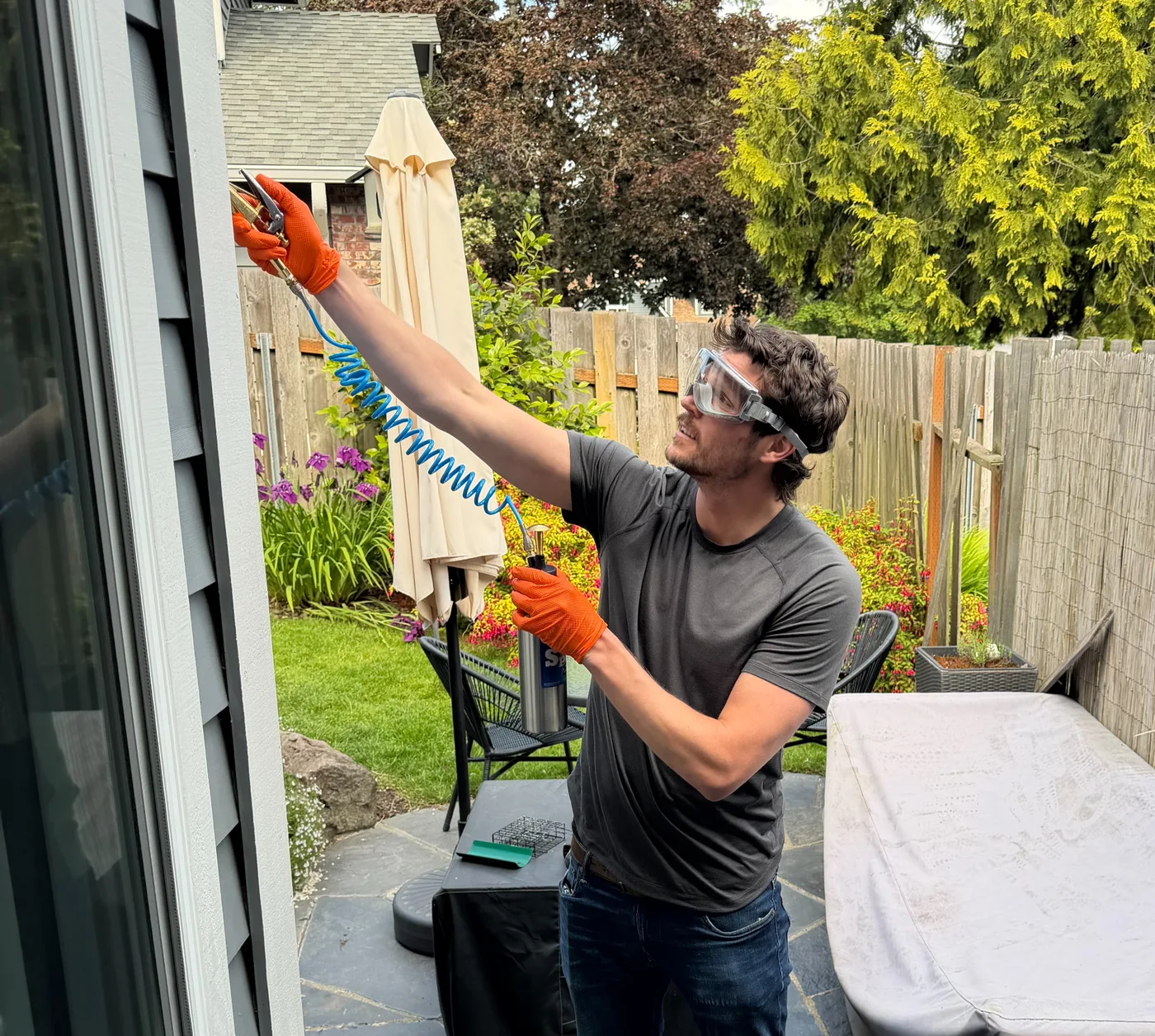 Sam in goggles and orange gloves treating the top edge of a window frame on a back patio