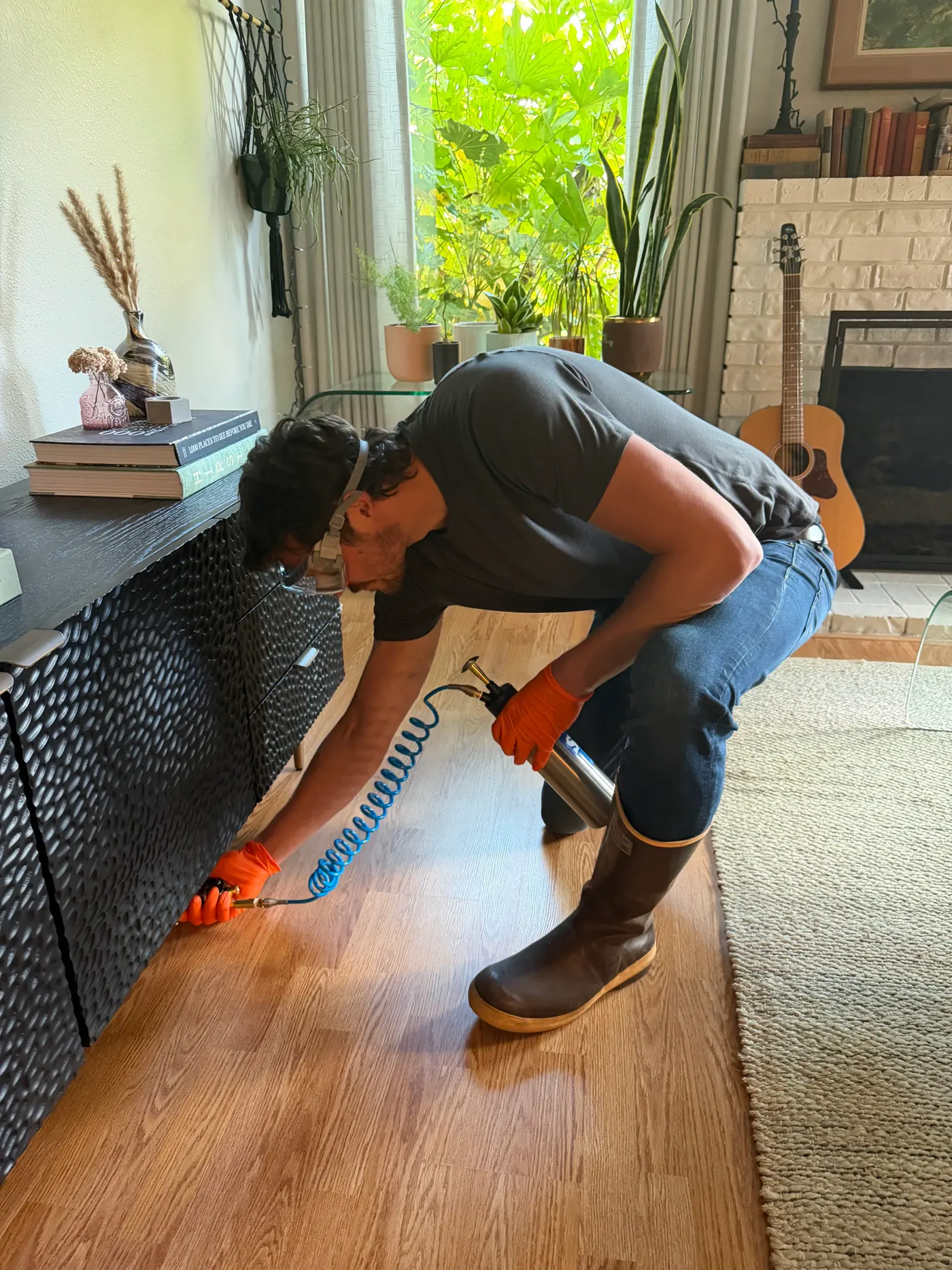 Sam in a respirator and orange gloves spraying along an indoor baseboard during interior pest control treatment