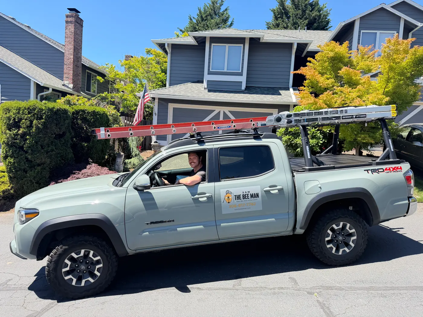 Sam seated in his branded Sam The Bee Man pickup truck carrying two extension ladders on a rack